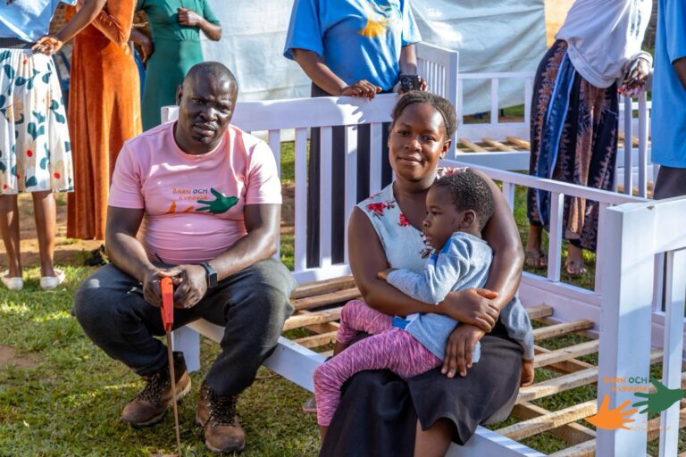 A team member sits with a family beside their new bed.