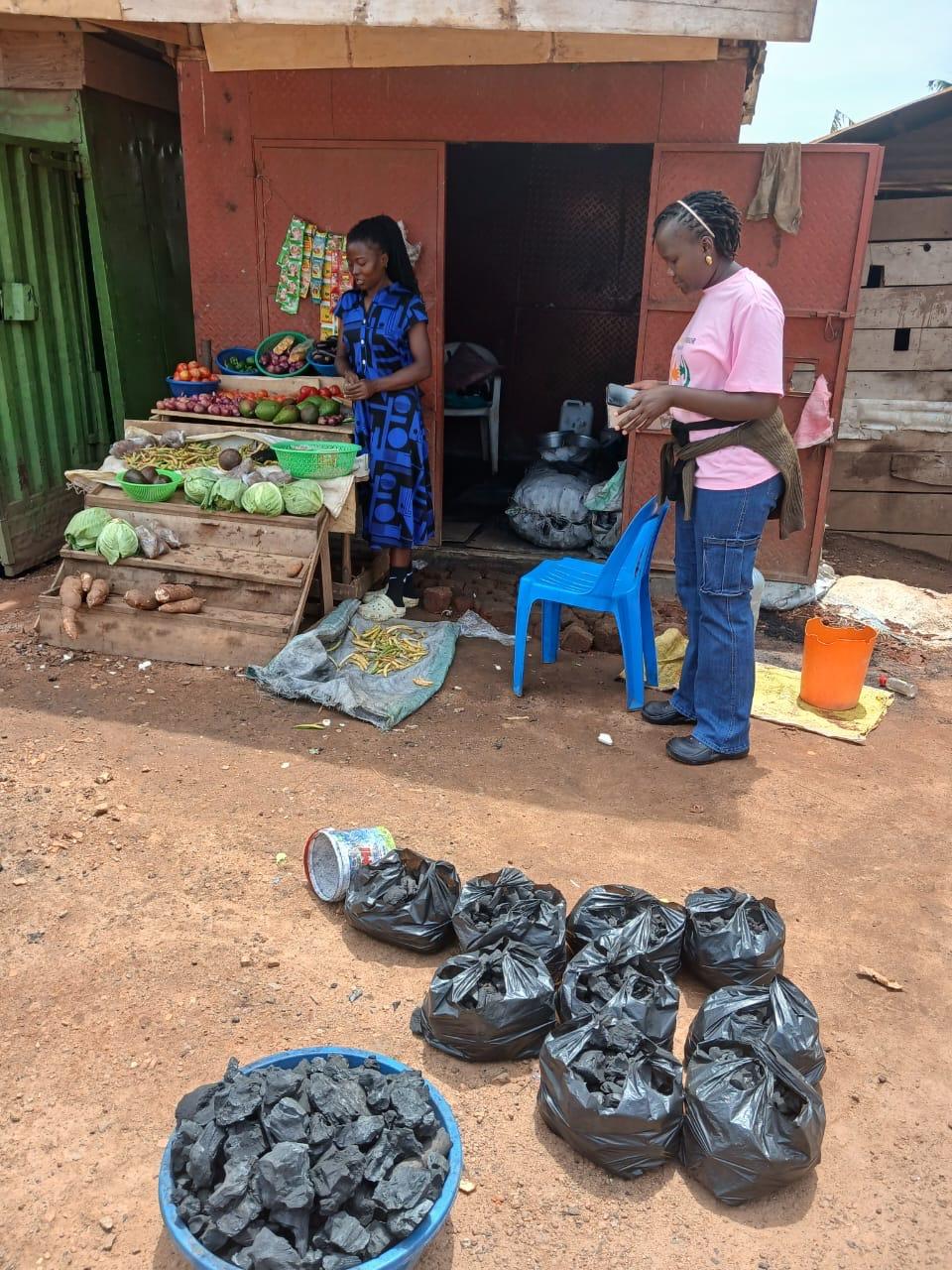 Two women at a produce stall with bags of charcoal in front