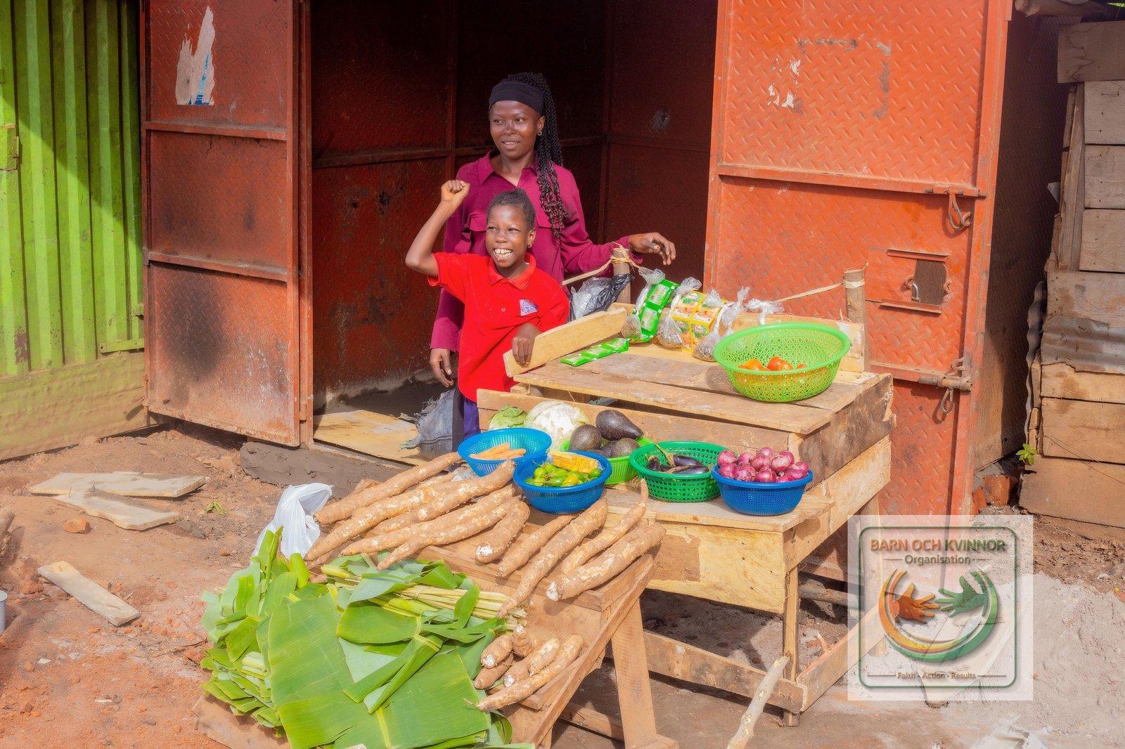 Mama Jennifer and her child at her stocked produce stall