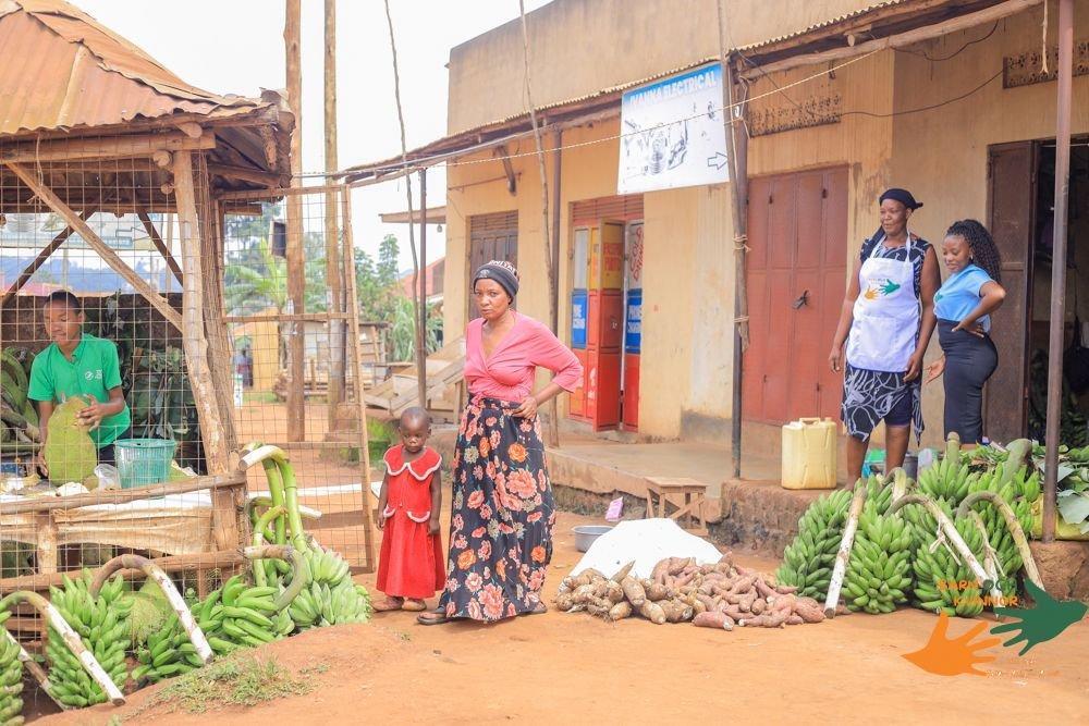 Women and children outside produce stalls and shops in a local market